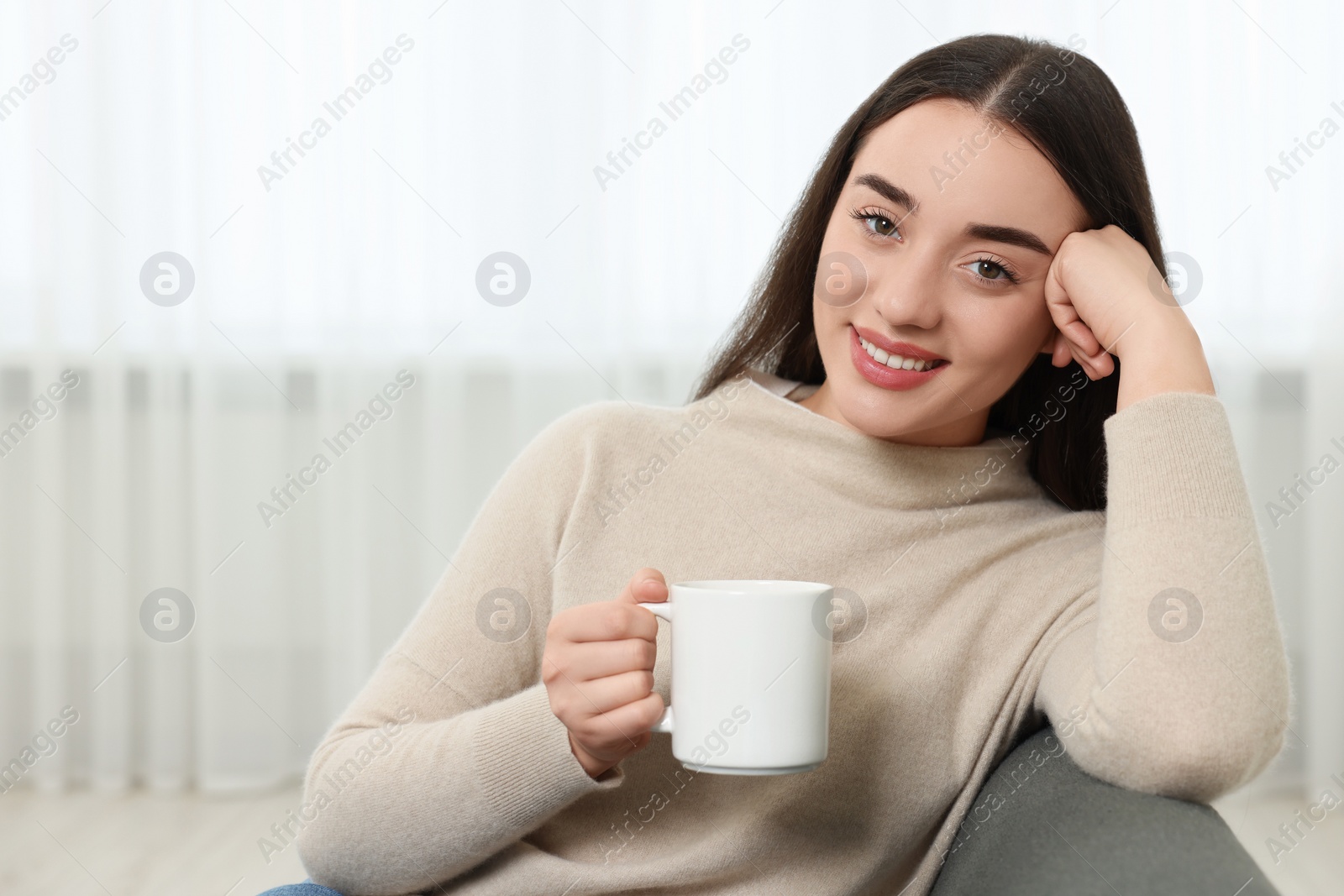 Photo of Happy young woman holding white ceramic mug at home