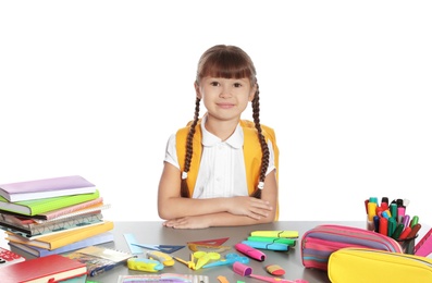 Cute girl sitting at table with school stationery against white background