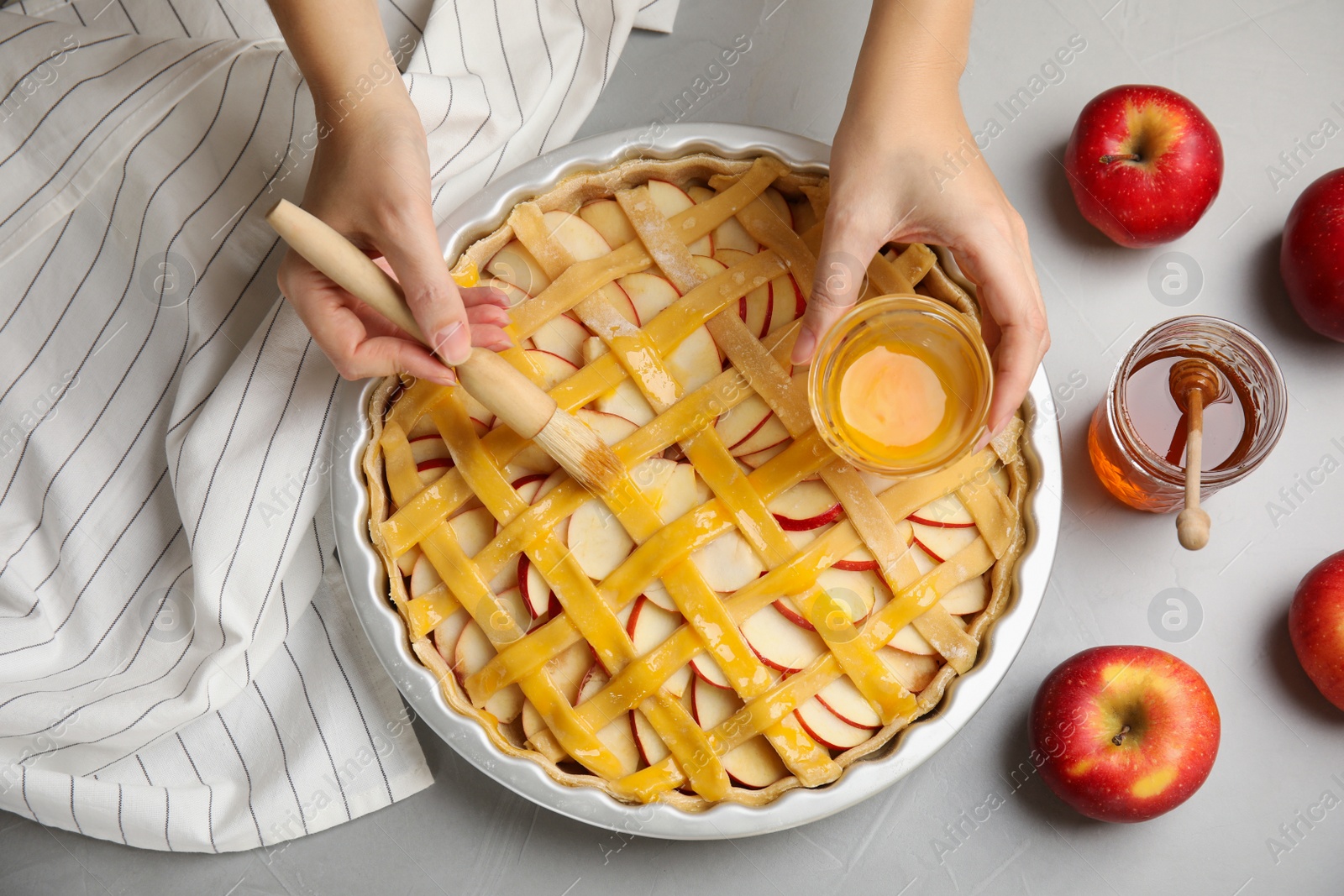 Photo of Woman applying liquid egg onto traditional English apple pie with brush at light grey table, top view