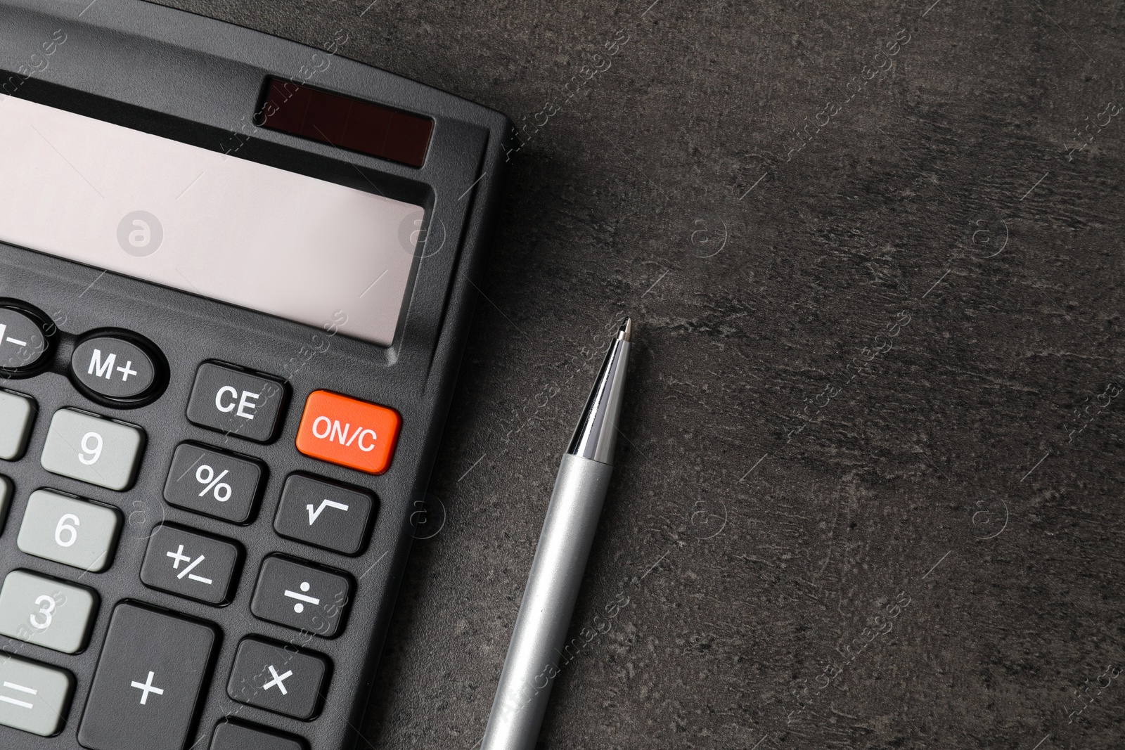 Photo of Calculator and pen on dark gray table, flat lay with space for text