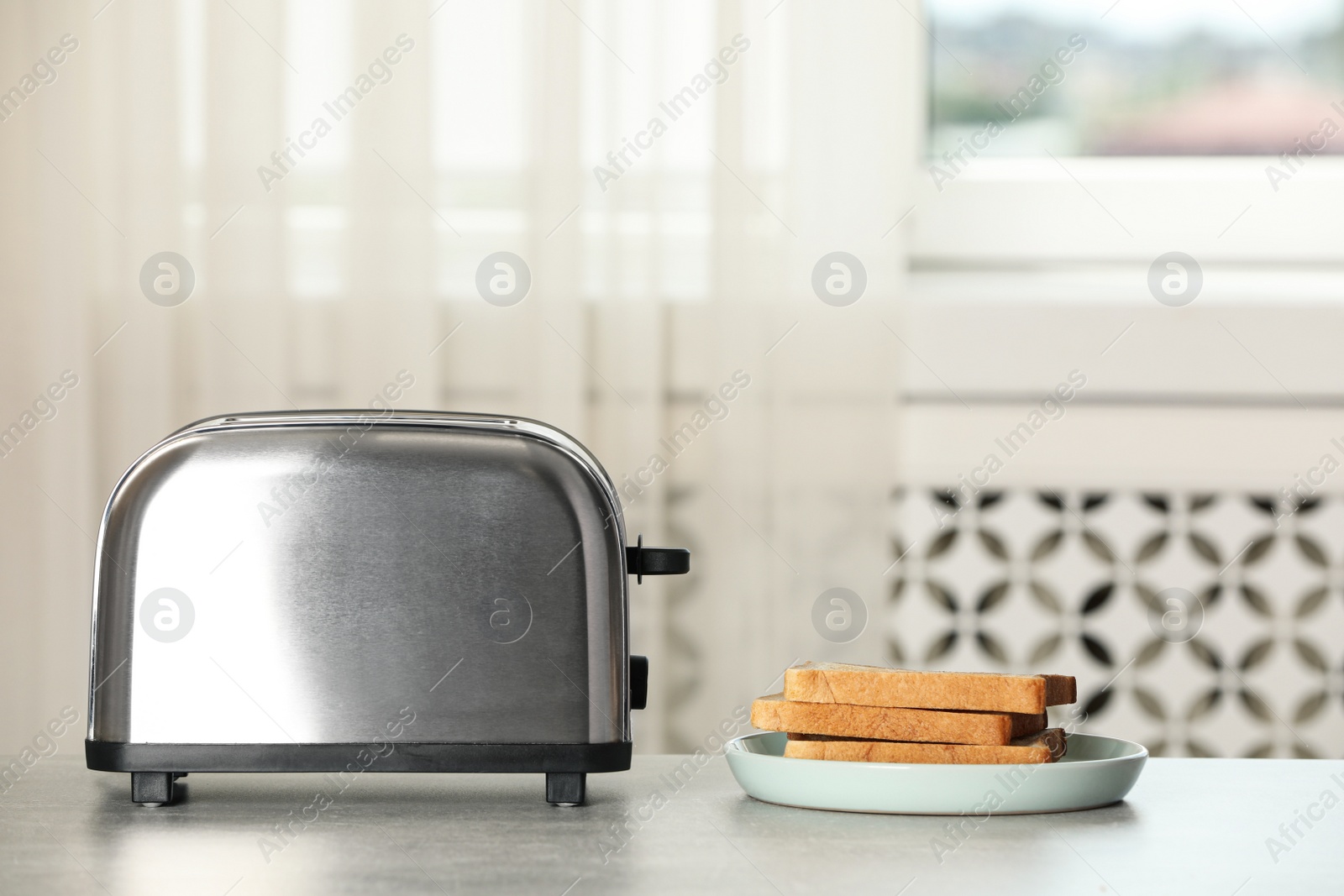 Photo of Electric toaster with bread slices on light table. Space for text