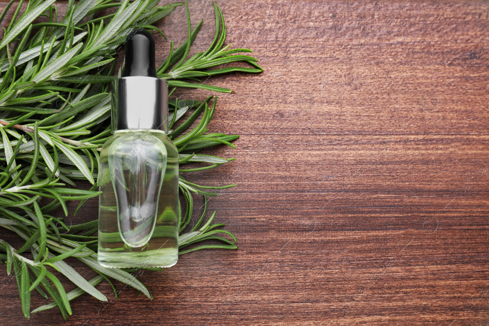 Photo of Bottle of rosemary essential oil on wooden table, flat lay. Space for text