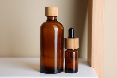 Photo of Glass bottles of cosmetic products on white shelf