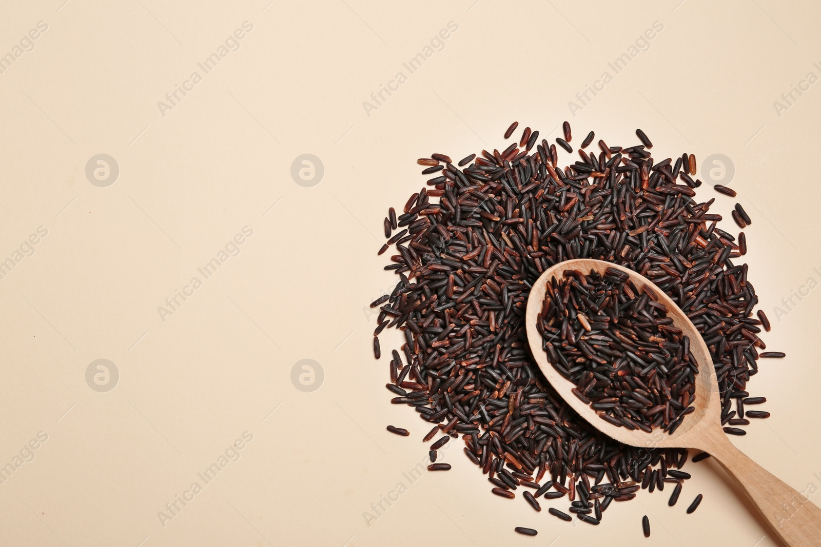 Photo of Black rice and wooden spoon on color background, top view Space for text