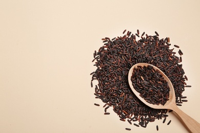 Photo of Black rice and wooden spoon on color background, top view Space for text