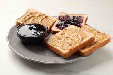 Photo of Delicious toasts with peanut butter and jam on white marble table