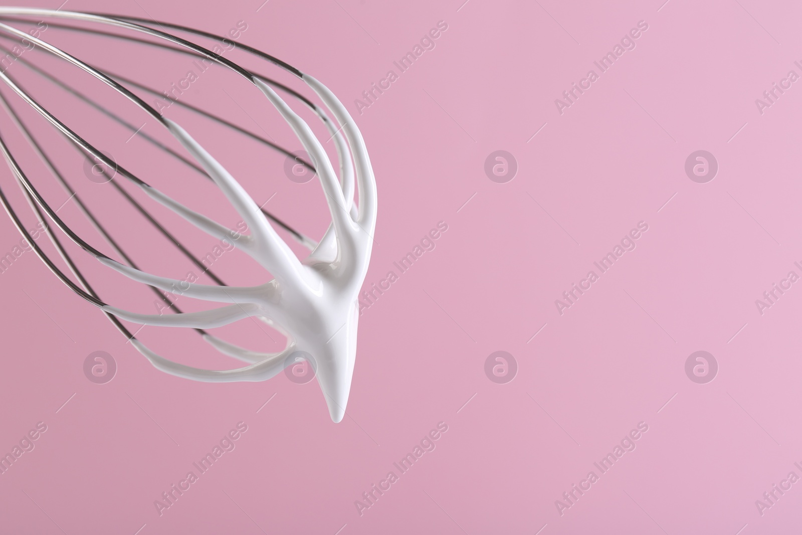 Photo of Whisk with whipped cream on pink background, closeup. Space for text