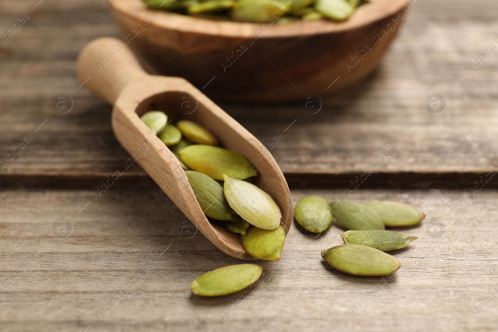 Photo of Scoop with peeled pumpkin seeds on wooden table, closeup