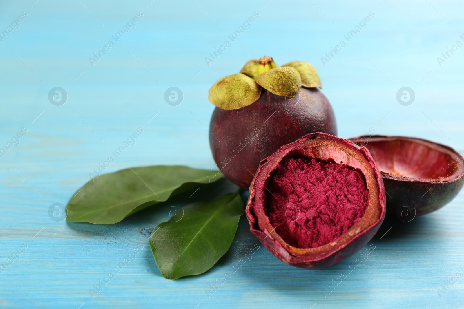 Photo of Purple mangosteen powder and fruits on light blue wooden table, closeup