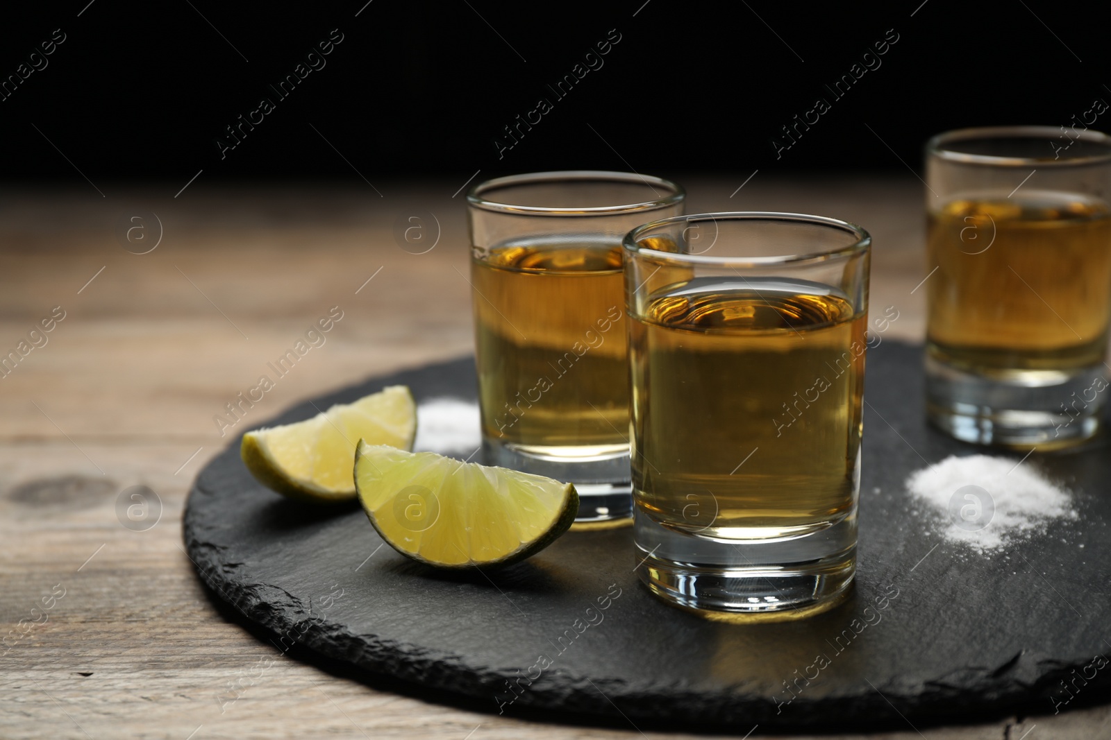 Photo of Mexican Tequila shots, lime slices and salt on wooden table