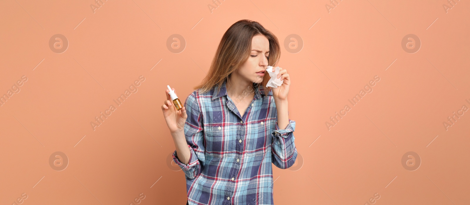 Photo of Sick young woman with nasal spray and tissue on coral background