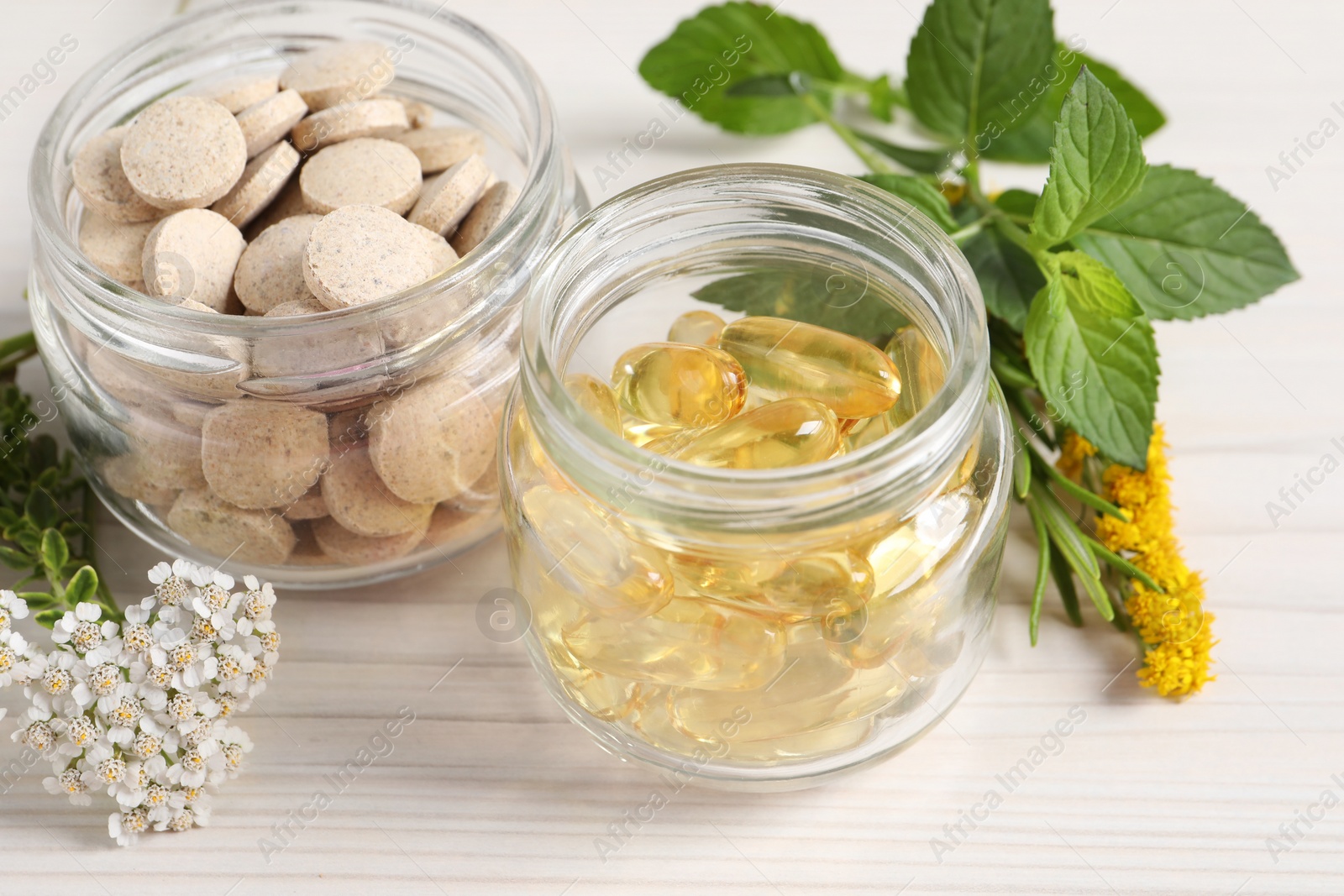 Photo of Jars with different pills, flowers and herbs on white wooden table, closeup. Dietary supplements