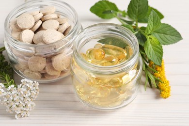 Jars with different pills, flowers and herbs on white wooden table, closeup. Dietary supplements
