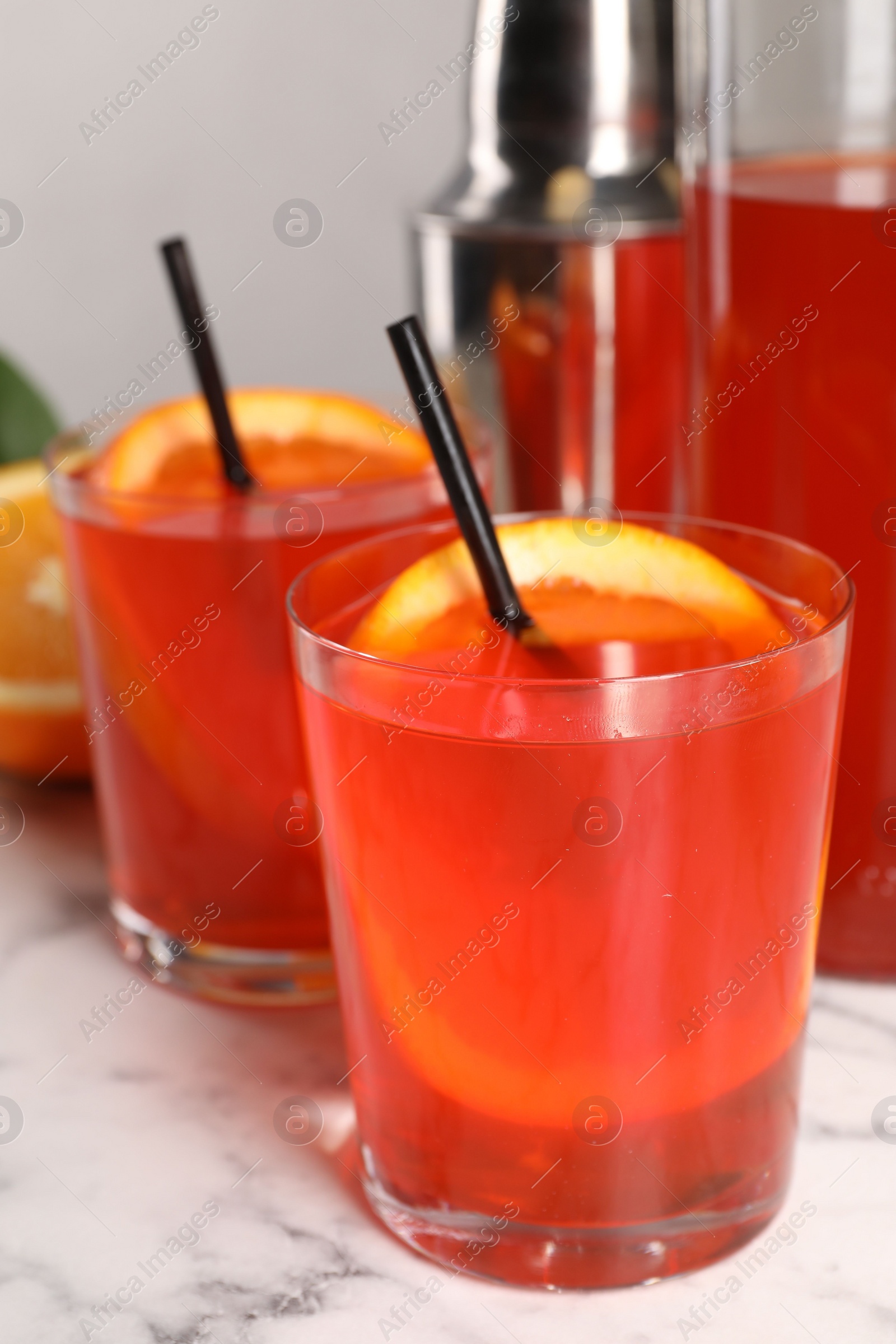 Photo of Aperol spritz cocktail, orange slices and straws in glasses on white marble table, closeup