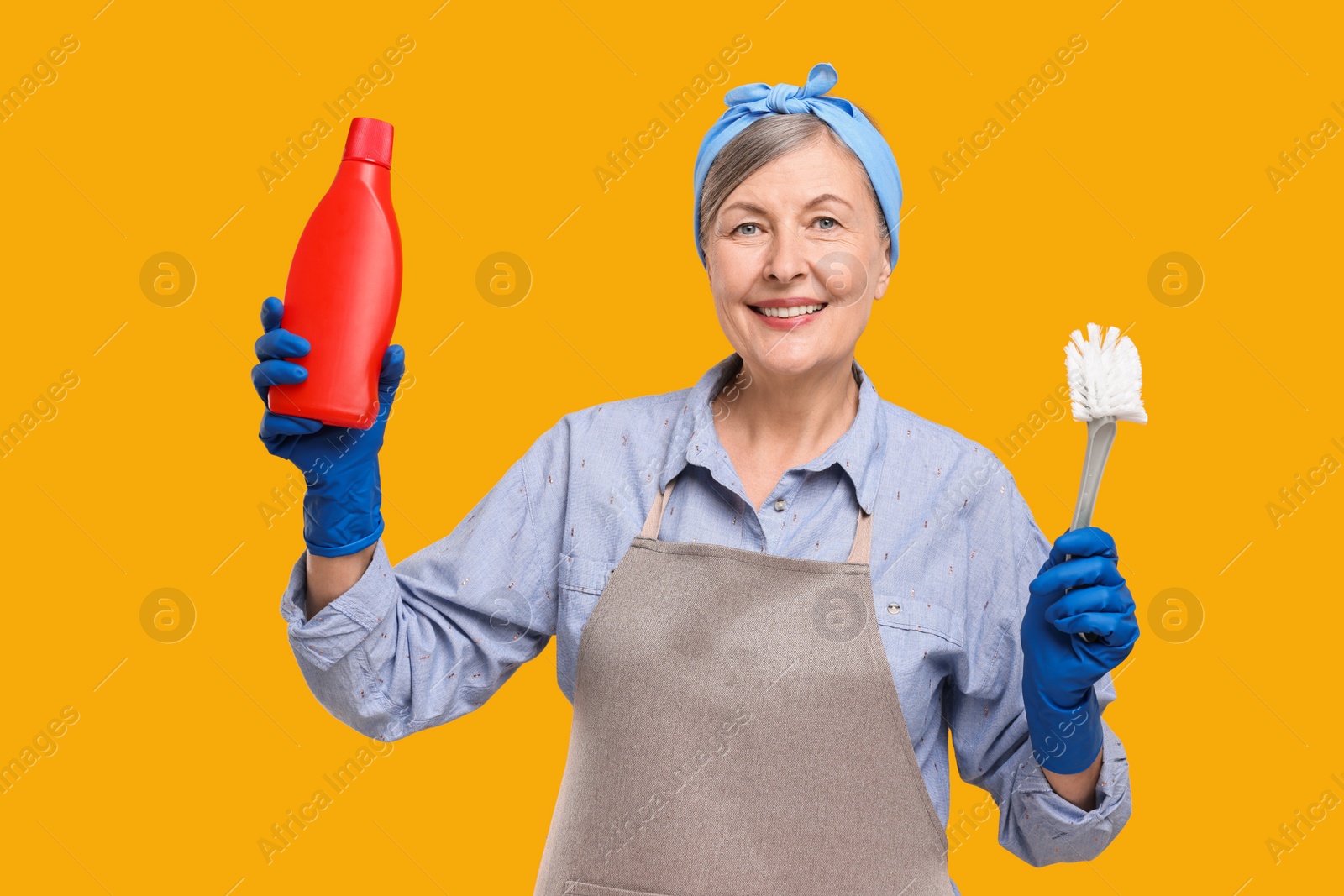 Photo of Happy housewife bottle of detergent and brush on orange background