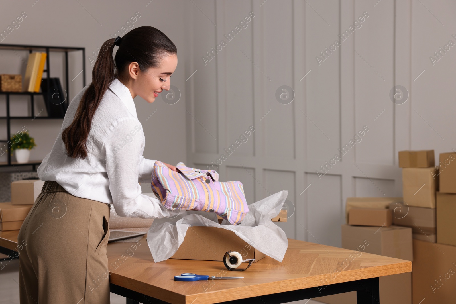 Photo of Seller packing shirt into cardboard box at table in office, space for text