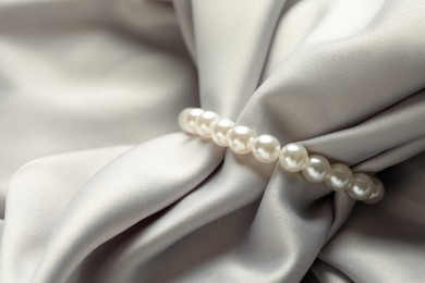 Photo of Elegant bracelet with pearls on grey silk, closeup