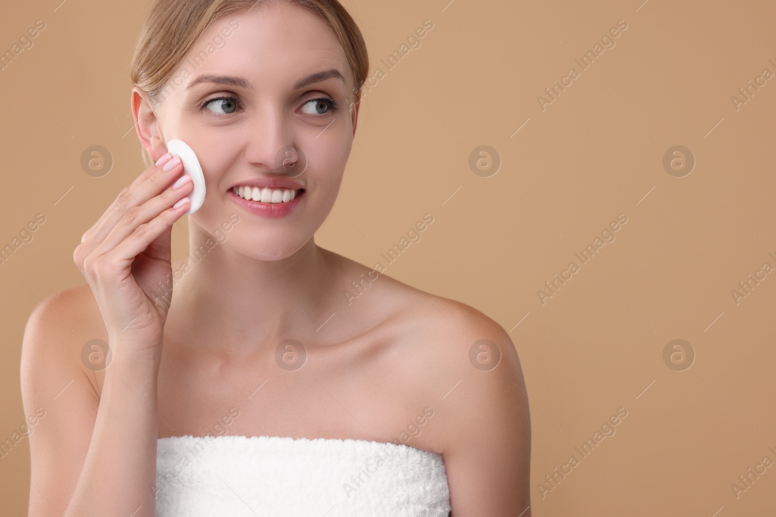 Photo of Young woman cleaning her face with cotton pad on beige background. Space for text