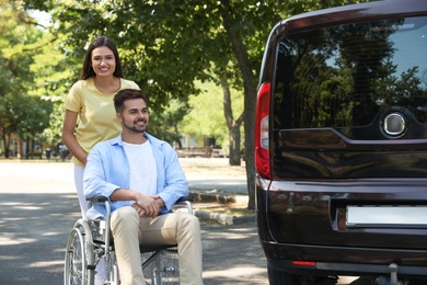 Photo of Young woman with man in wheelchair near van outdoors