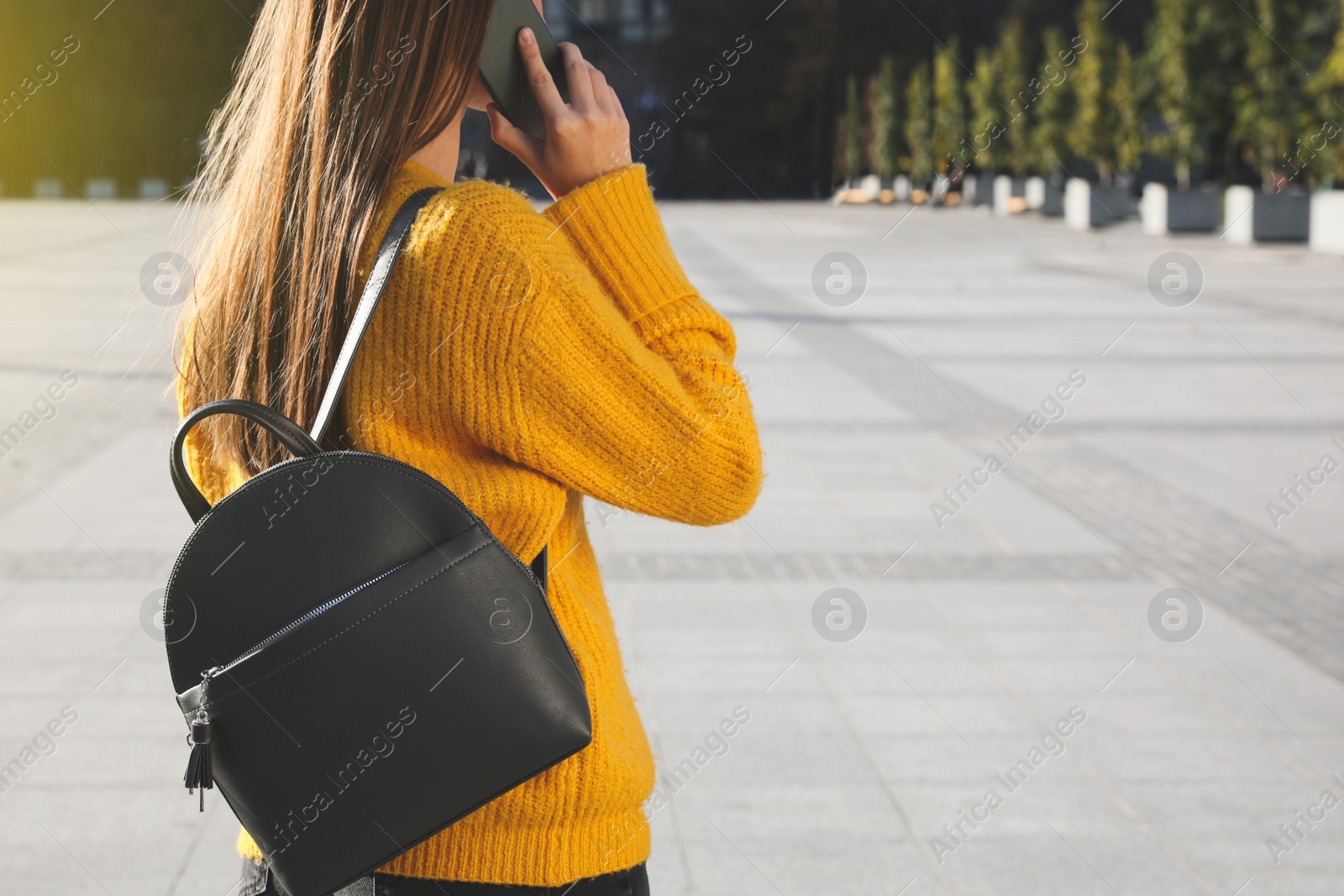 Photo of Young woman with stylish black backpack talking on phone outdoors, closeup. Space for text