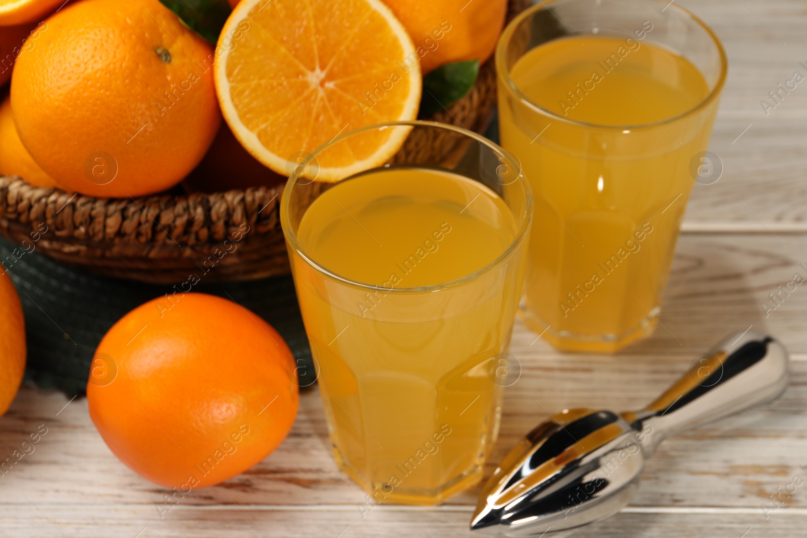 Photo of Many ripe juicy oranges, squeezer and fresh juice on white wooden table, closeup