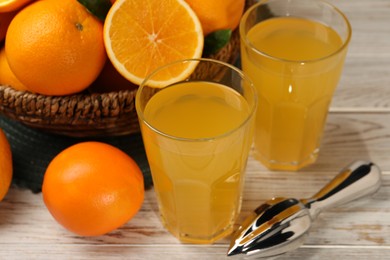 Photo of Many ripe juicy oranges, squeezer and fresh juice on white wooden table, closeup