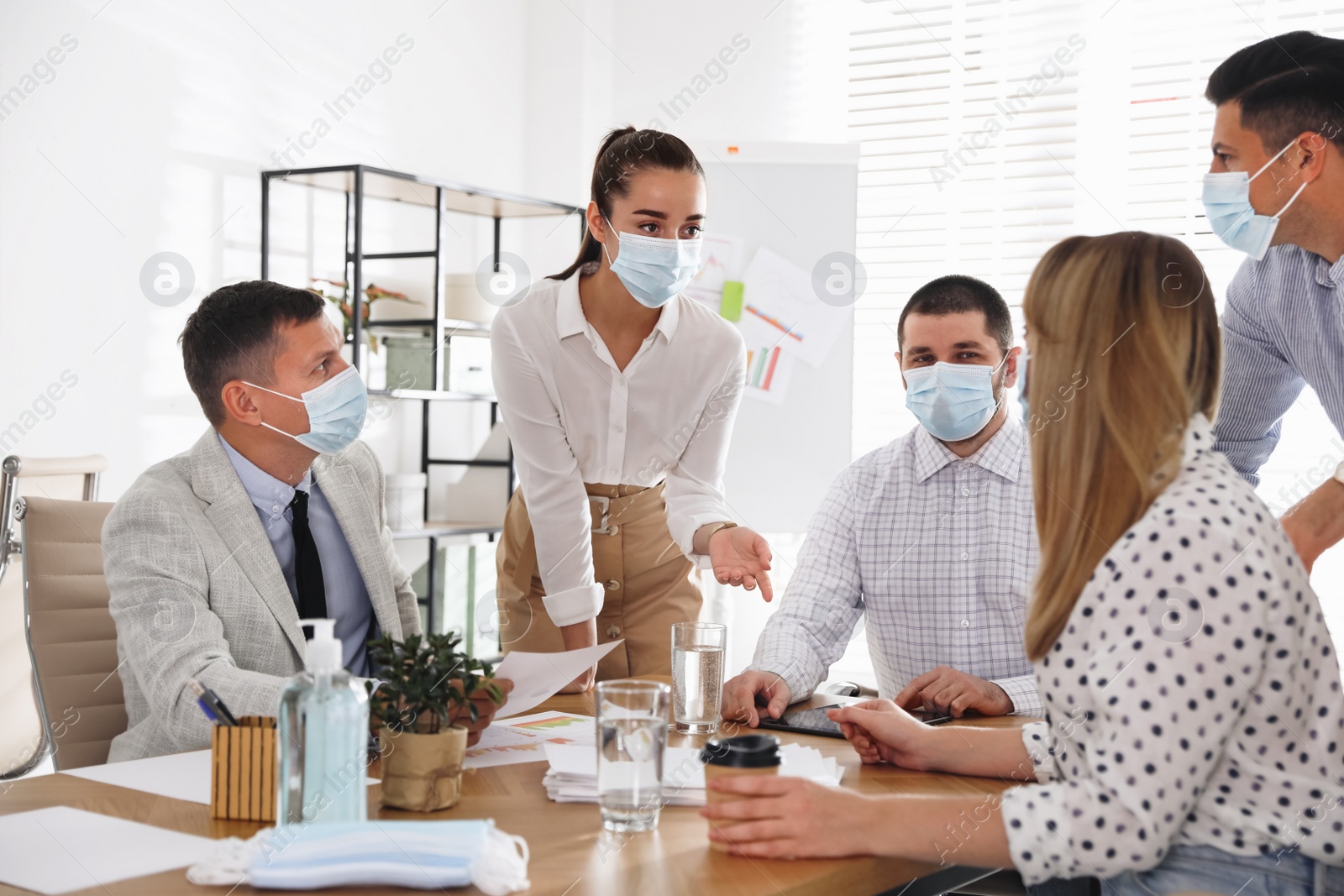 Photo of Group of coworkers with protective masks in office. Business meeting during COVID-19 pandemic