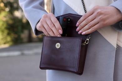 Photo of Young woman putting pepper spray into bag outdoors, closeup