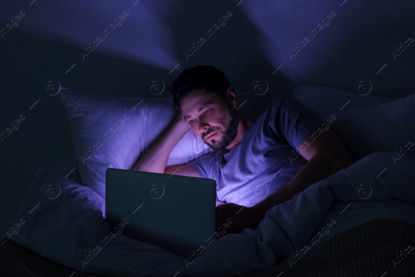 Photo of Man using laptop in bed at night. Internet addiction