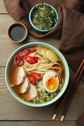 Photo of Delicious ramen in bowl, soy sauce and microgreens on wooden table, flat lay. Noodle soup