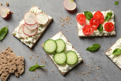 Tasty snacks with cream cheese and vegetables on gray table, flat lay