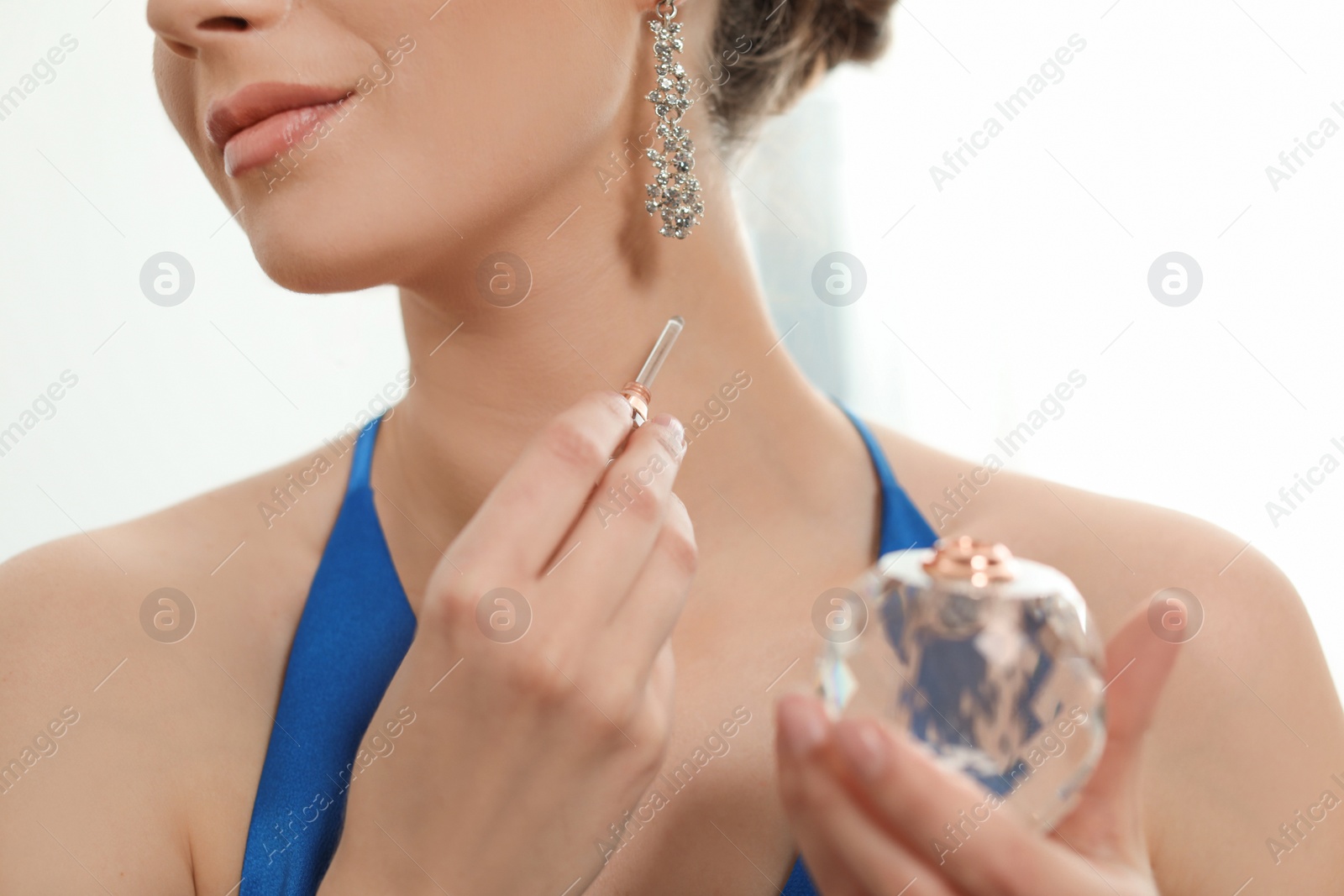 Photo of Young woman applying perfume on neck against light background, closeup