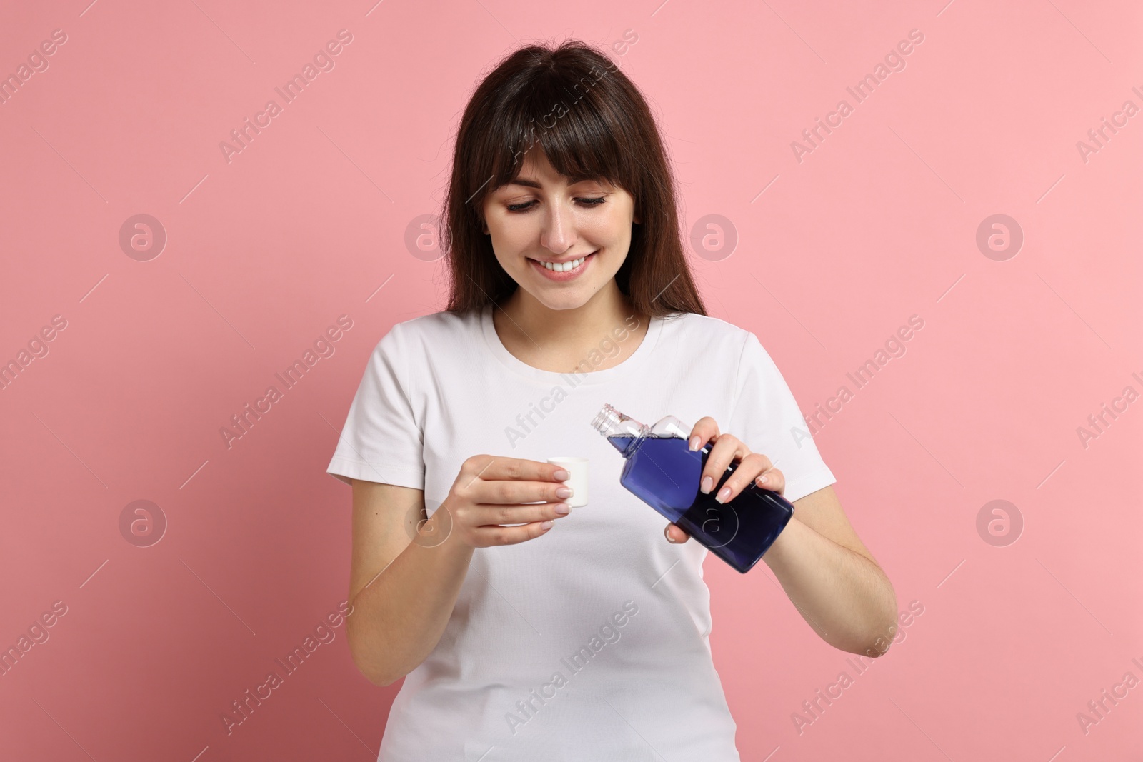 Photo of Young woman using mouthwash on pink background