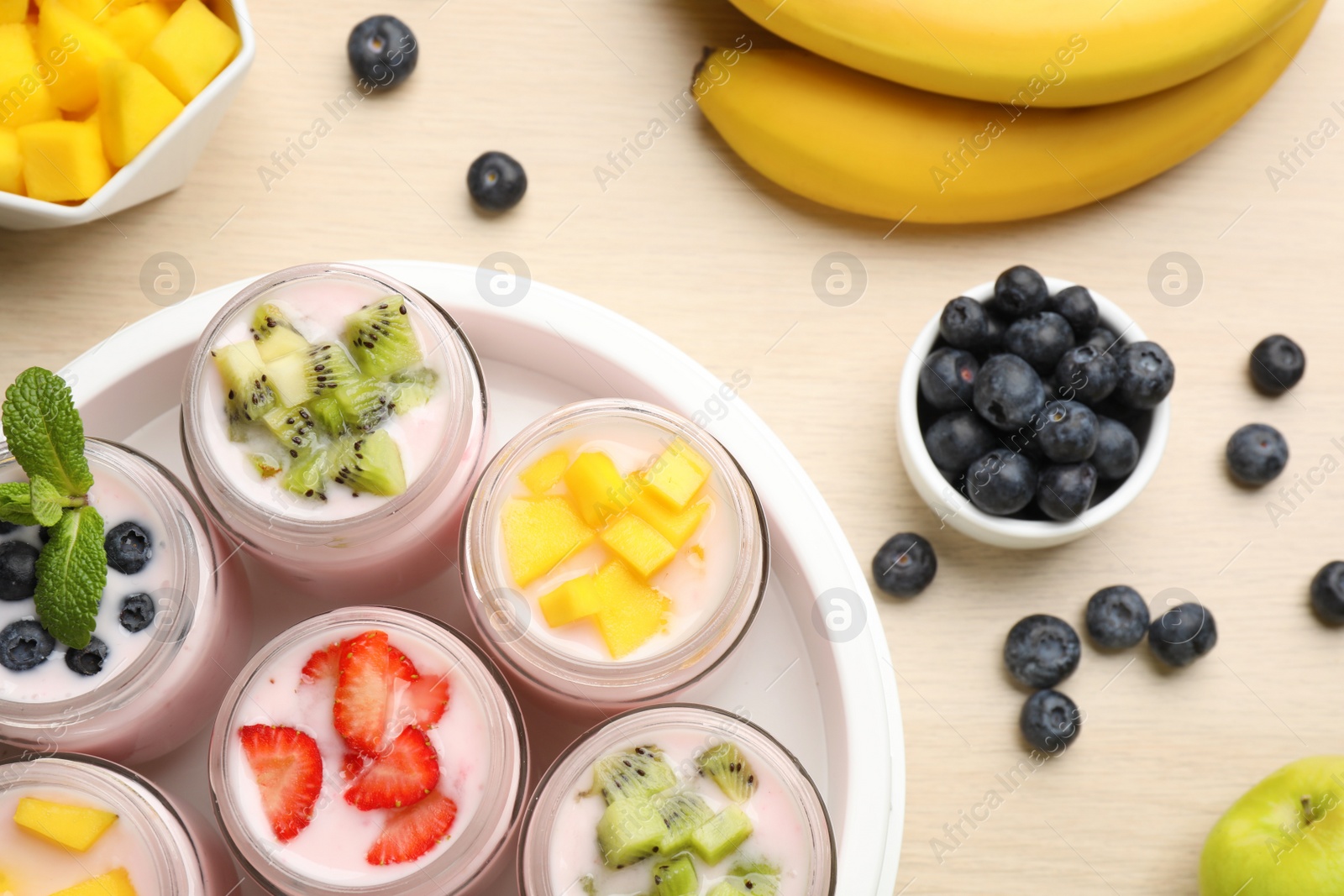 Photo of Yogurt maker with jars and different fruits on wooden table, flat lay