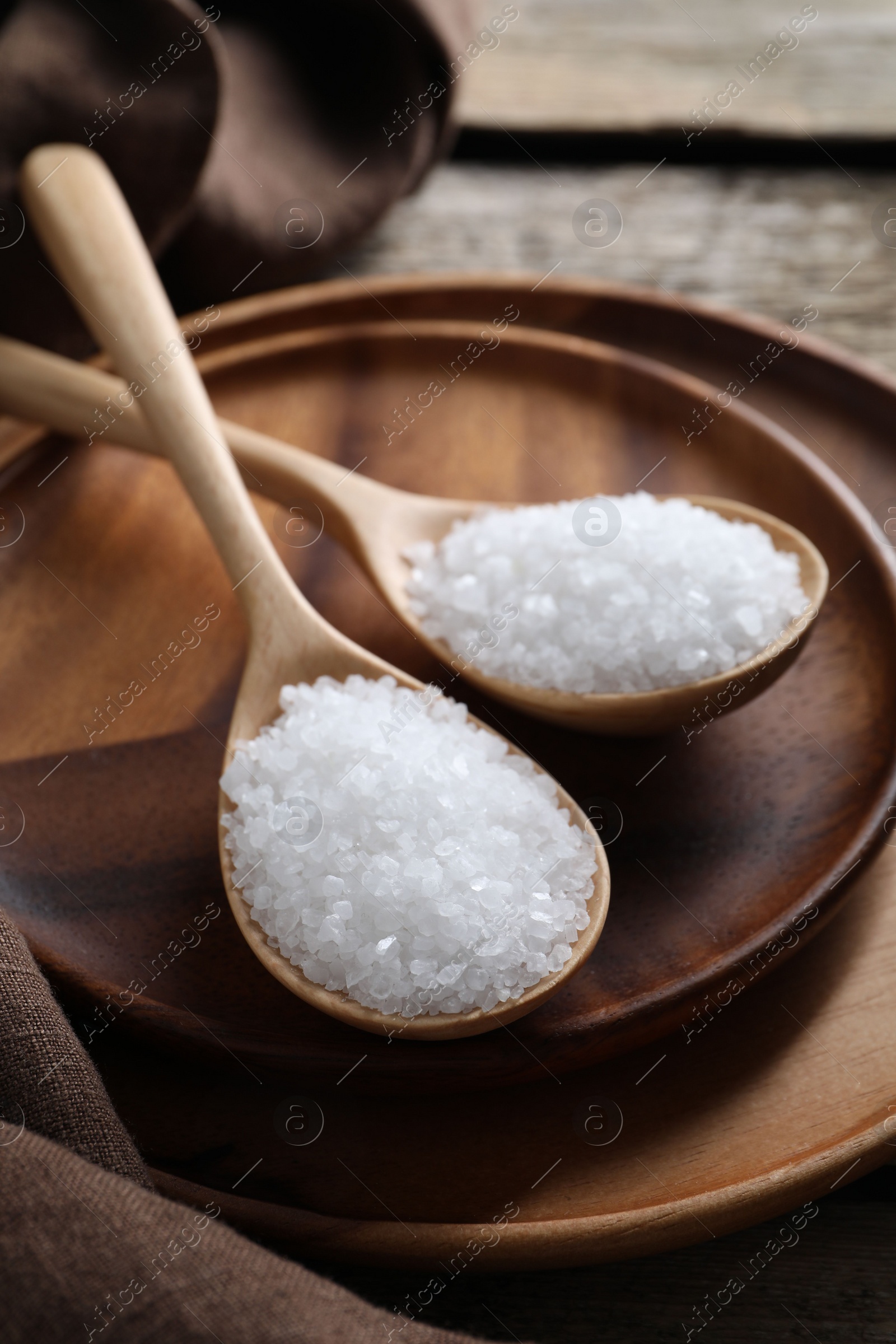 Photo of Organic salt in spoons on wooden table, closeup