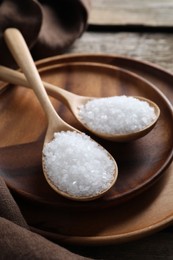 Photo of Organic salt in spoons on wooden table, closeup