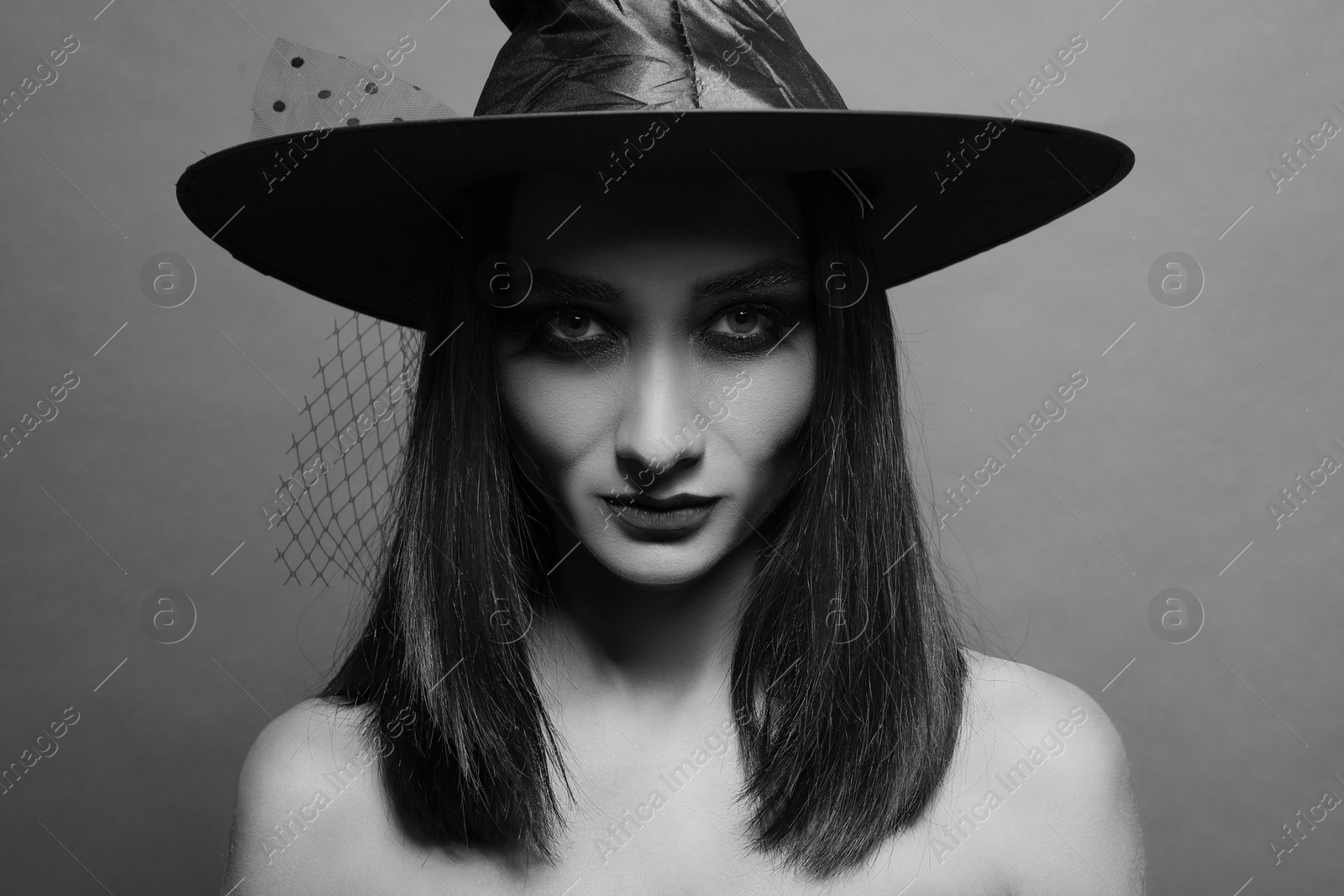 Photo of Mysterious witch wearing hat on dark background. Black and white effect