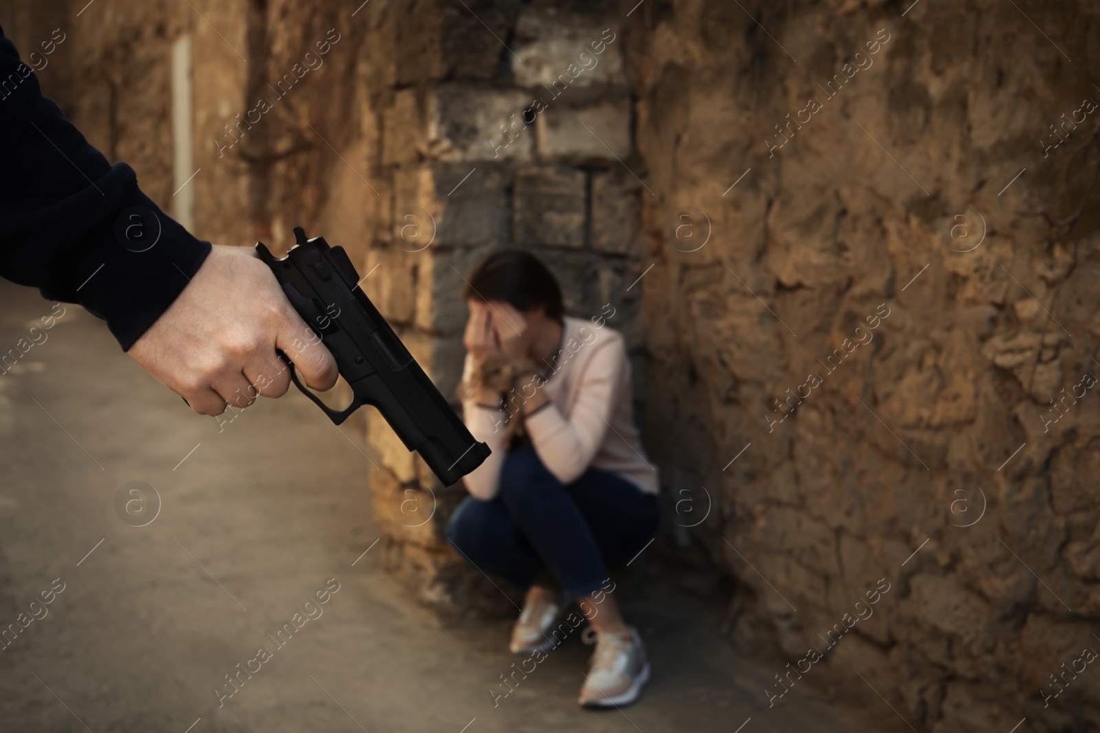 Photo of Armed man holding woman hostage outdoors, focus on hand with gun. Criminal offence