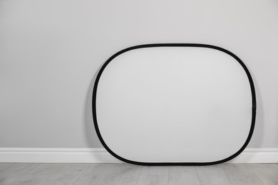 Studio reflector near grey wall in room, space for text. Professional photographer's equipment