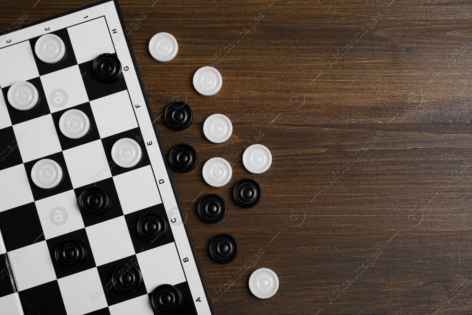 Photo of Checkerboard and game pieces on wooden table, flat lay. Space for text