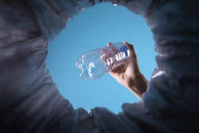 Photo of Bottom view of woman throwing plastic bottle into trash bin on light blue background, closeup