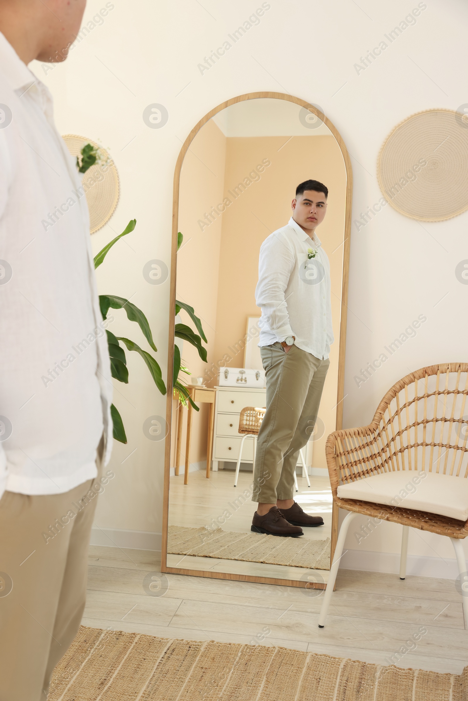 Photo of Young groom preparing for wedding near mirror indoors