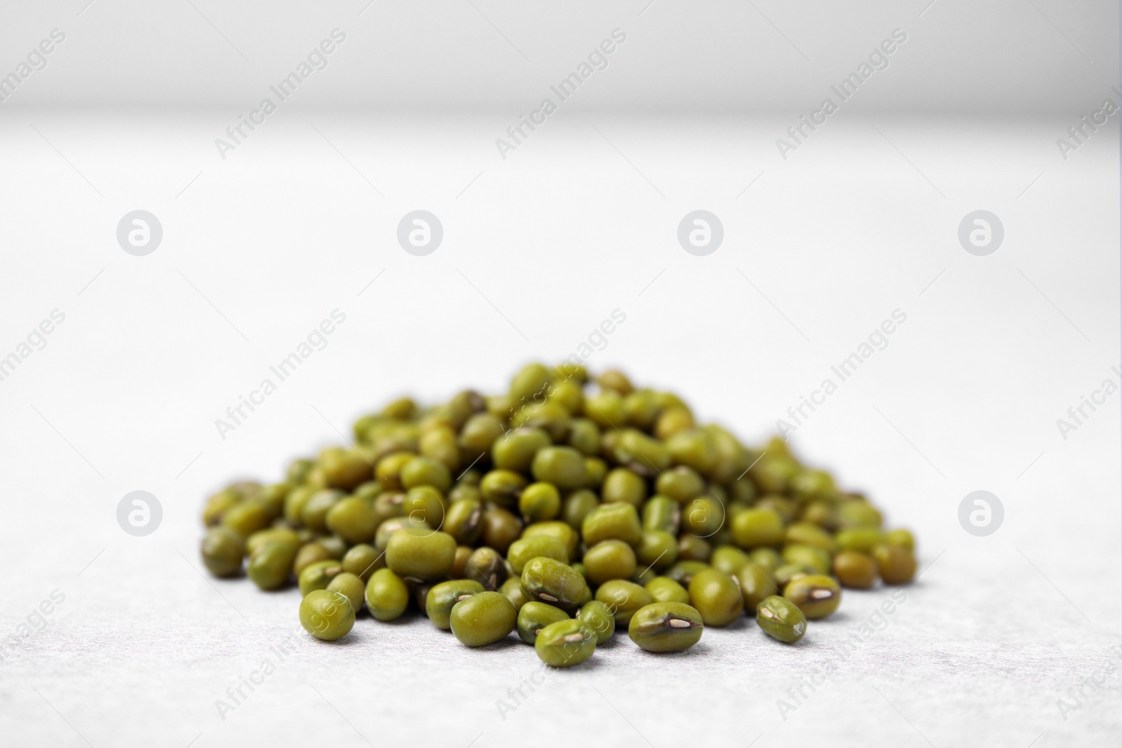 Photo of Pile of green mung beans on light grey table, closeup