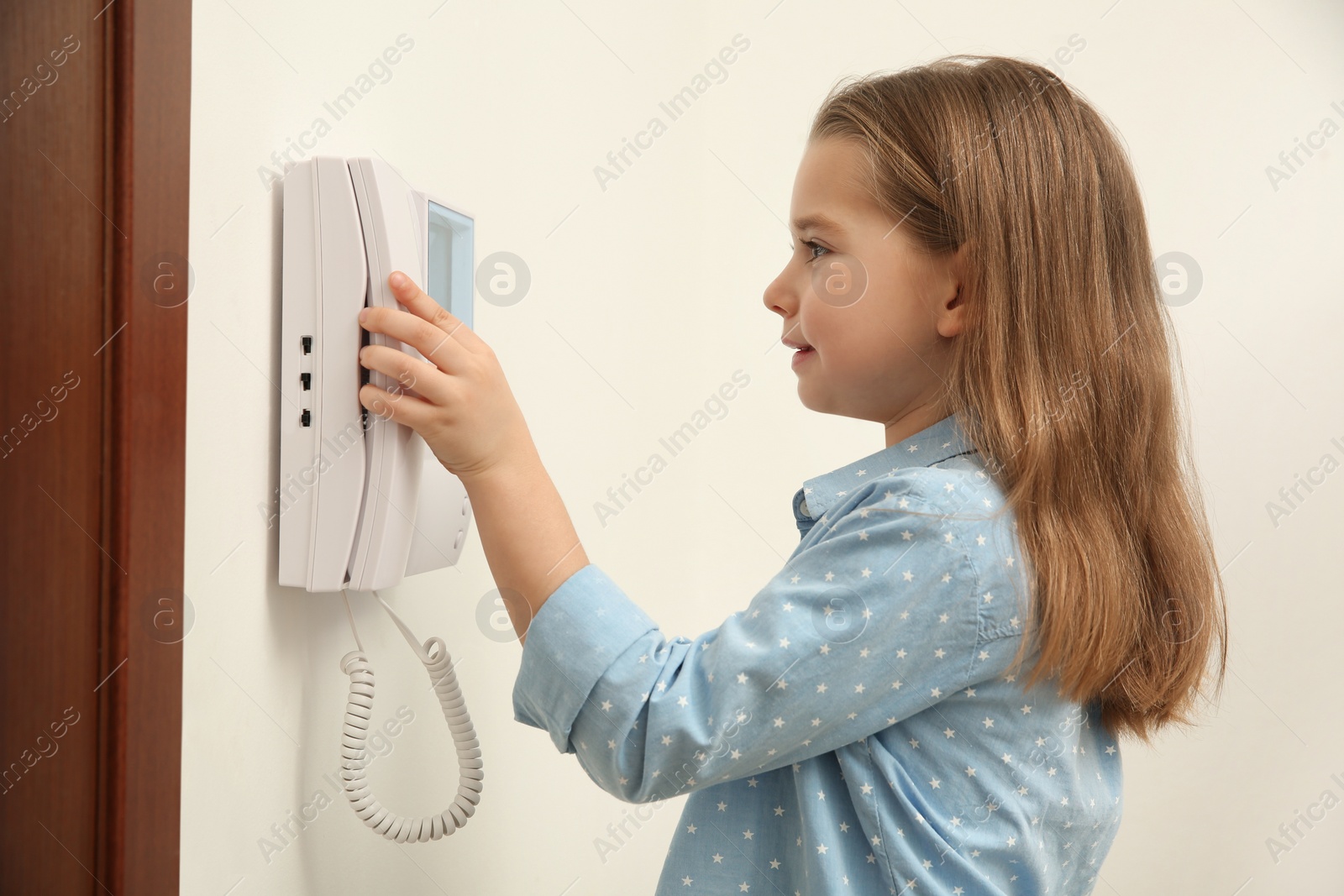 Photo of Cute little girl answering intercom call indoors