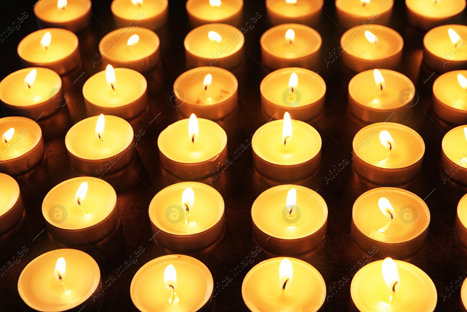 Photo of Wax candles burning on table in darkness, closeup