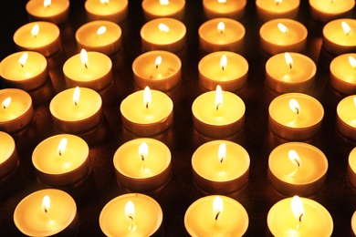 Wax candles burning on table in darkness, closeup