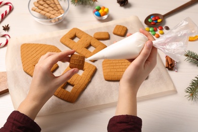 Woman making gingerbread house at white table, closeup
