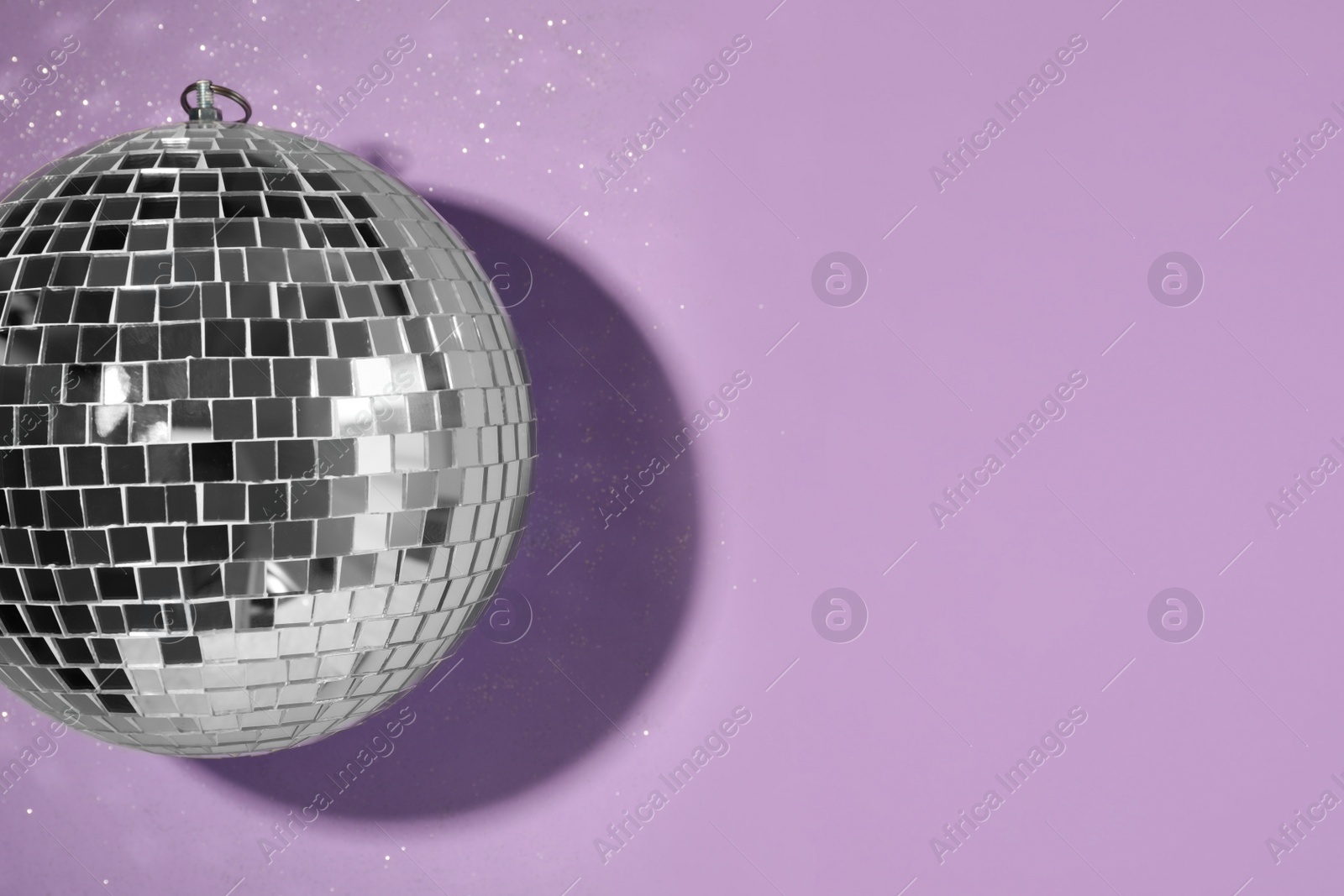Photo of Bright shiny disco ball on violet background, top view. Space for text