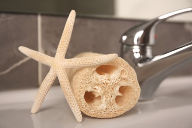 Photo of Natural loofah sponge and starfish on washbasin in bathroom, closeup