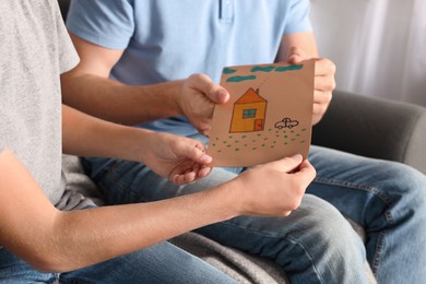 Photo of Happy man receiving greeting card from his son at home, closeup